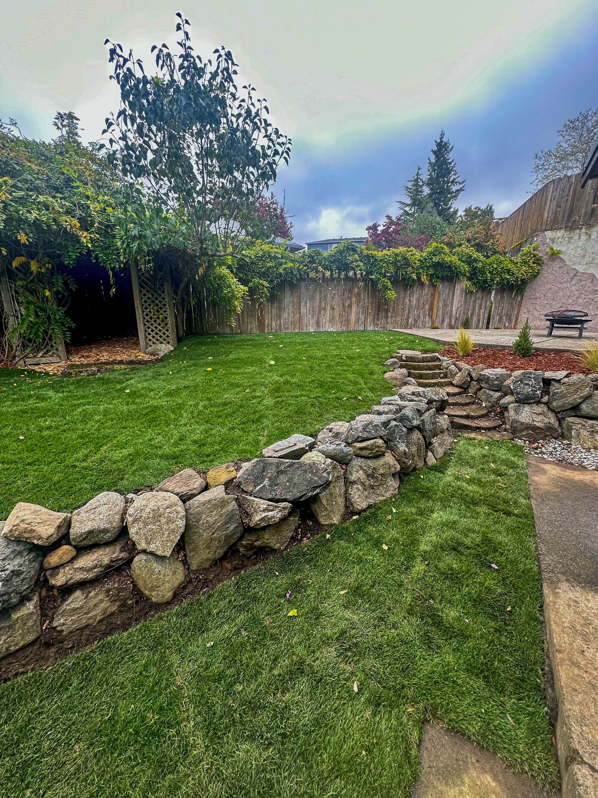 A stone wall surrounds a lush green lawn in a backyard.