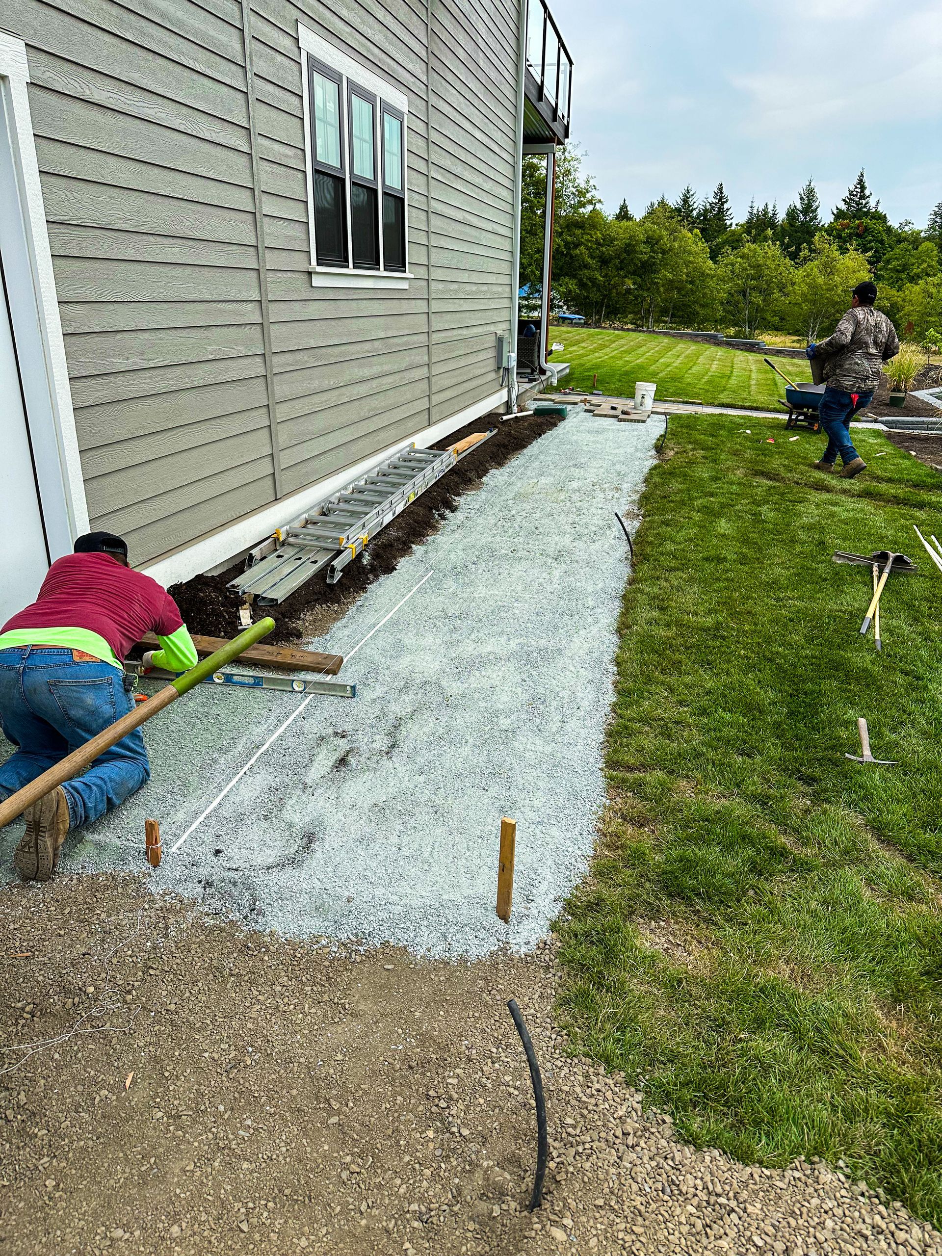 A couple of people are working on a sidewalk in front of a house.