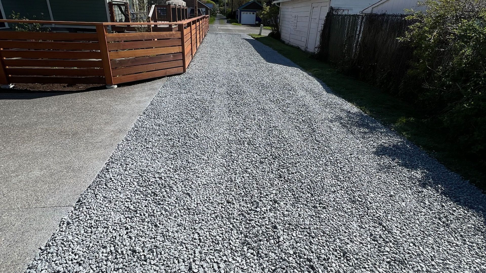 A gravel driveway flanked by a wooden fence and a building with green grass on either side.