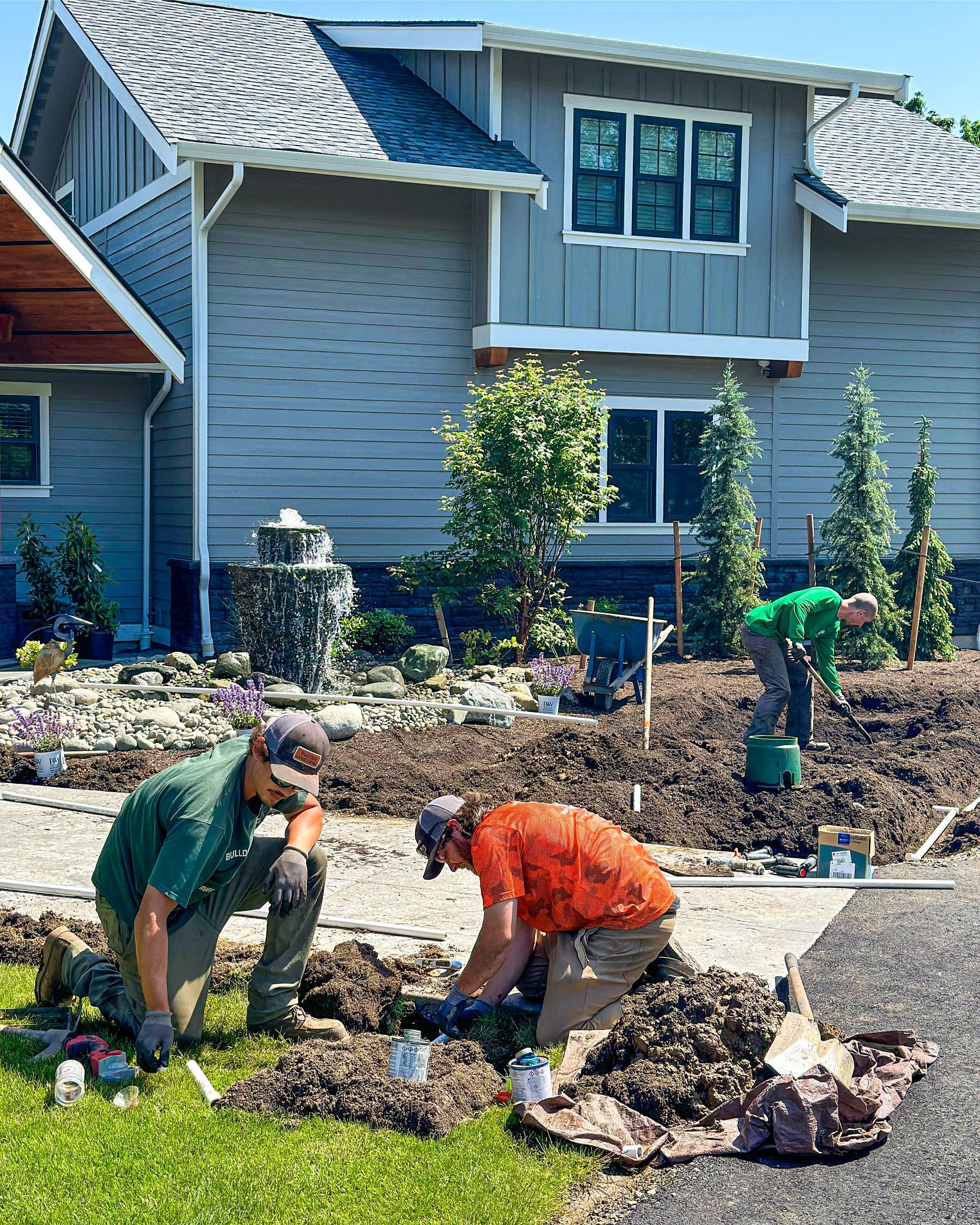 Two men are digging in the dirt in front of a house