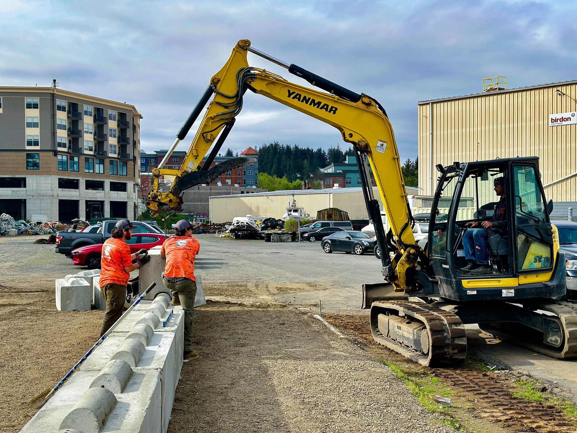 A man is standing next to a yellow excavator in a parking lot