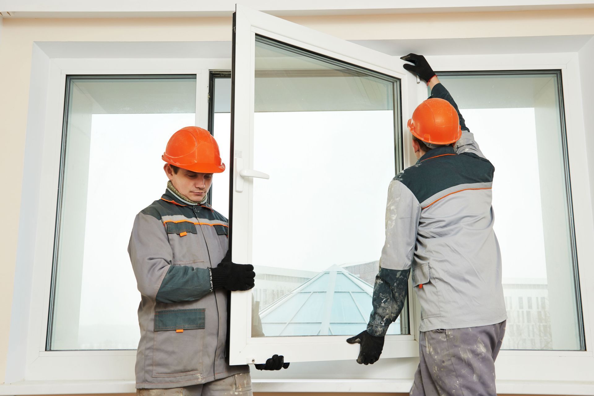 Two workers in hard hats installing a window.