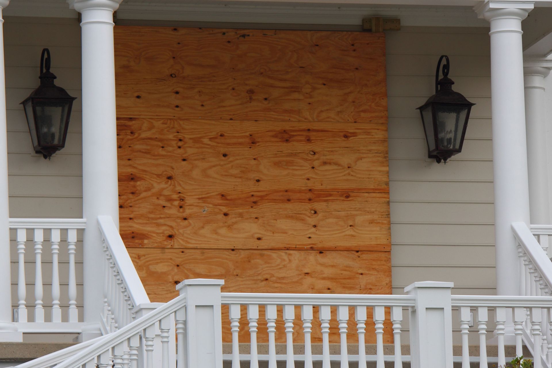 Exterior of house with plywood covering a window, flanked by lanterns.