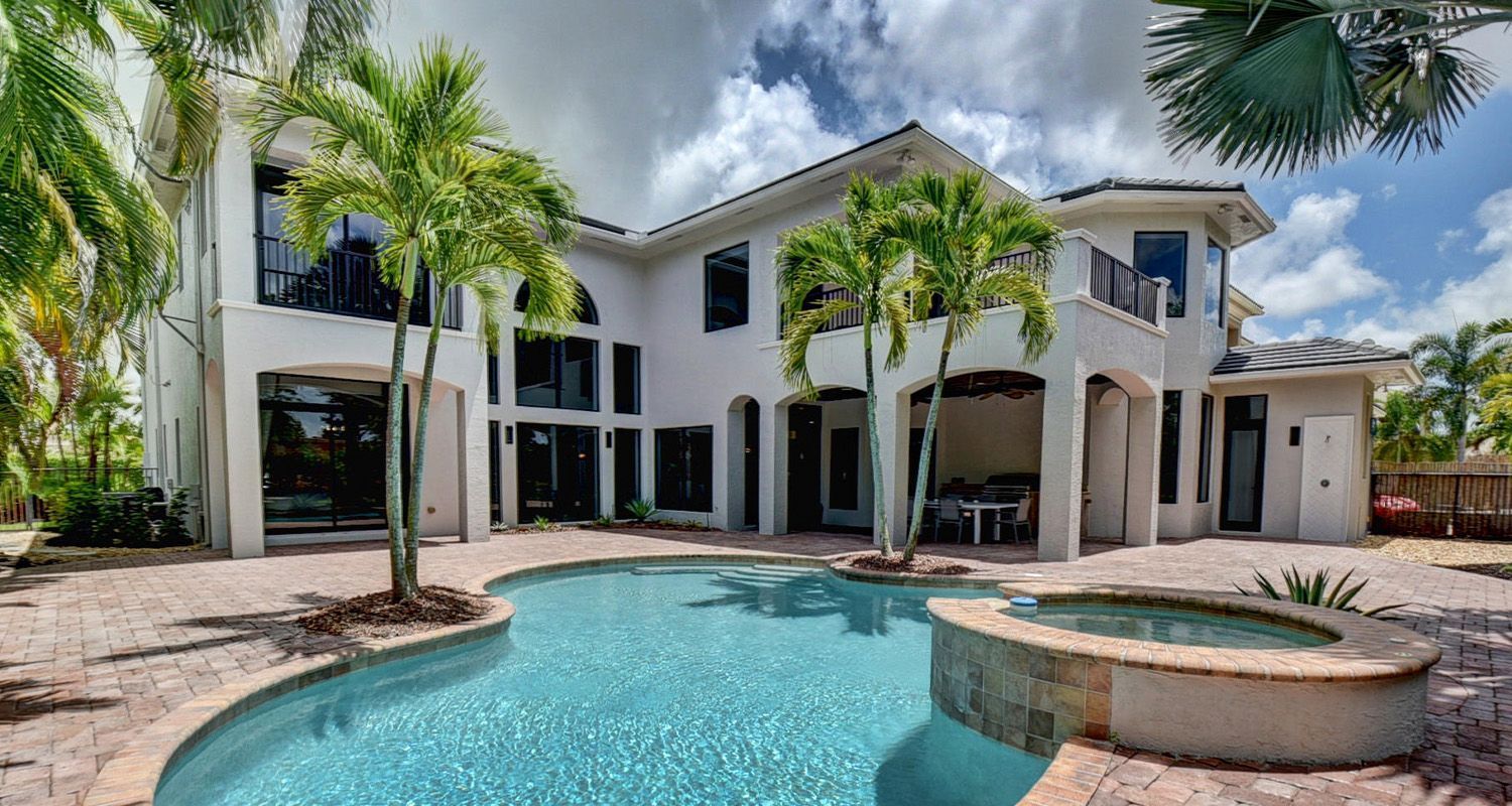 Large white house with a pool and palm trees under a cloudy sky.