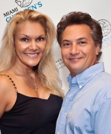 Woman with blonde hair and man in blue shirt smiling, posing in front of a Miami Children’s Hospital backdrop.