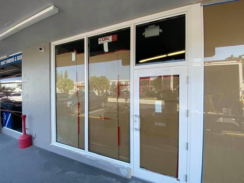 Storefront with white framed windows and a door, protected by cardboard. Exterior, daytime.