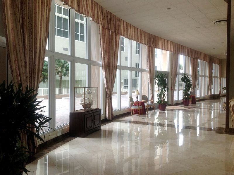 Bright hallway with large windows, tan curtains, and marble floor. A dark wooden cabinet sits below a window.