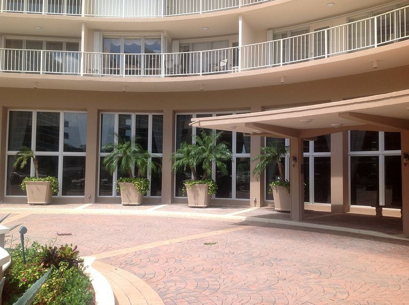 Building entrance with large windows, potted plants, and circular driveway.