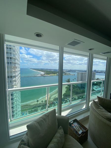 View from a high-rise window, overlooking a beach, bridge, and ocean on a sunny day.