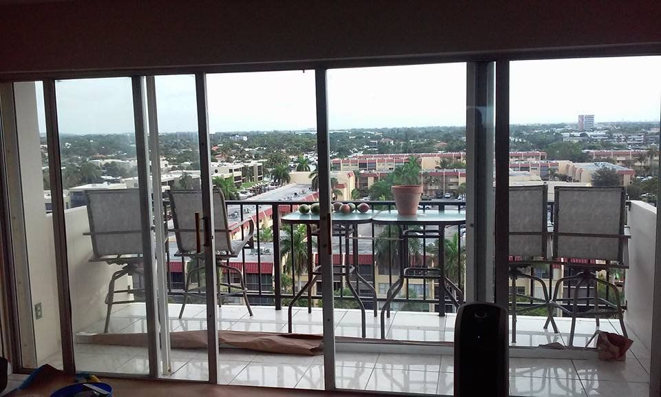 Balcony view through glass doors: outdoor seating, city buildings, cloudy sky.