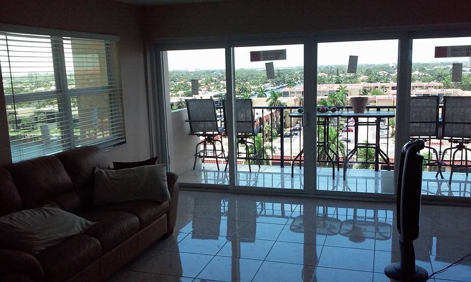 Living room with view: brown leather sofa, large windows to balcony with chairs, city view.