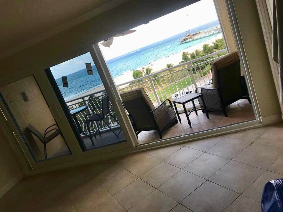 Balcony overlooking ocean, chairs and table visible. Bright day, blue water and sky.