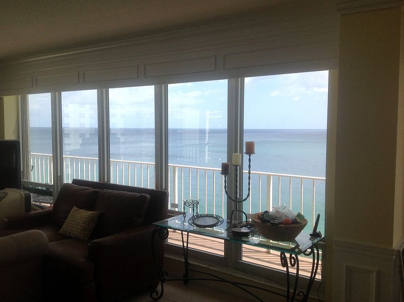 Living room with large windows overlooking the ocean. Brown sofa, glass table, and candle holder.