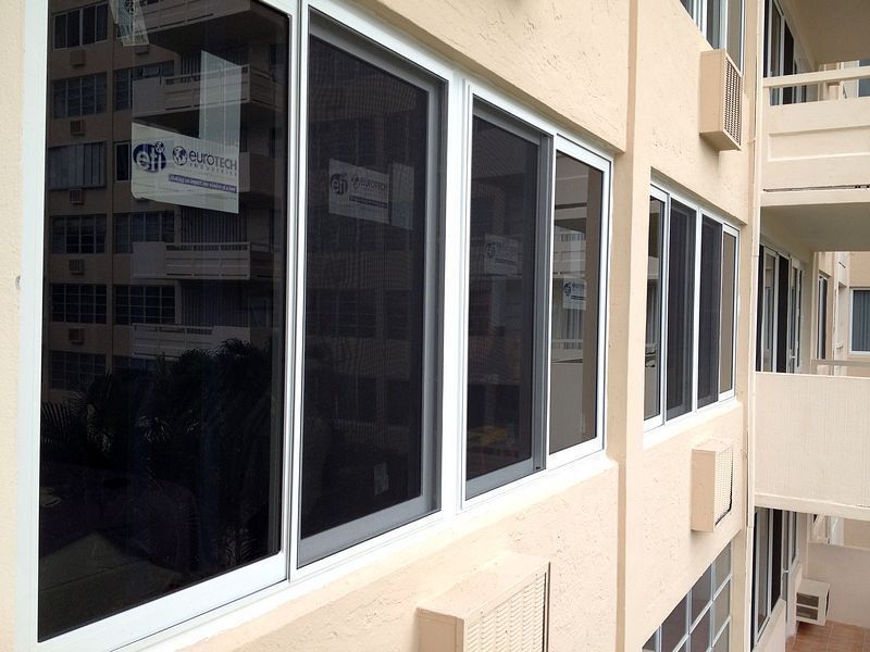 Building exterior with multiple windows; some open, with dark screens; beige walls.