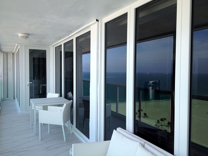 Balcony with white furniture and floor-to-ceiling windows overlooking the ocean.