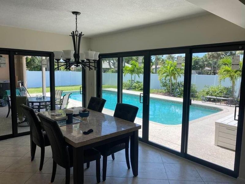 Dining room with table and chairs, overlooking a swimming pool through large sliding glass doors.