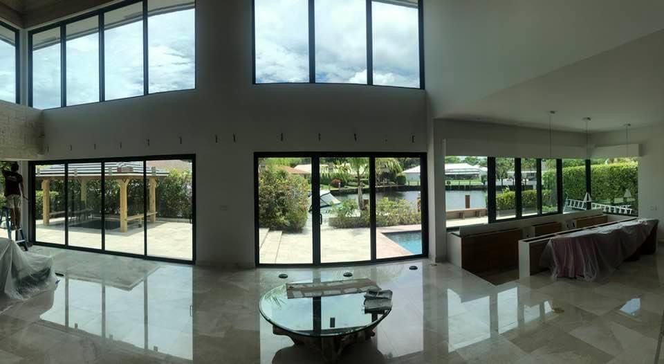 Spacious, modern room with large windows overlooking a backyard with pool. Foldable glass doors and a reflective glass coffee table.