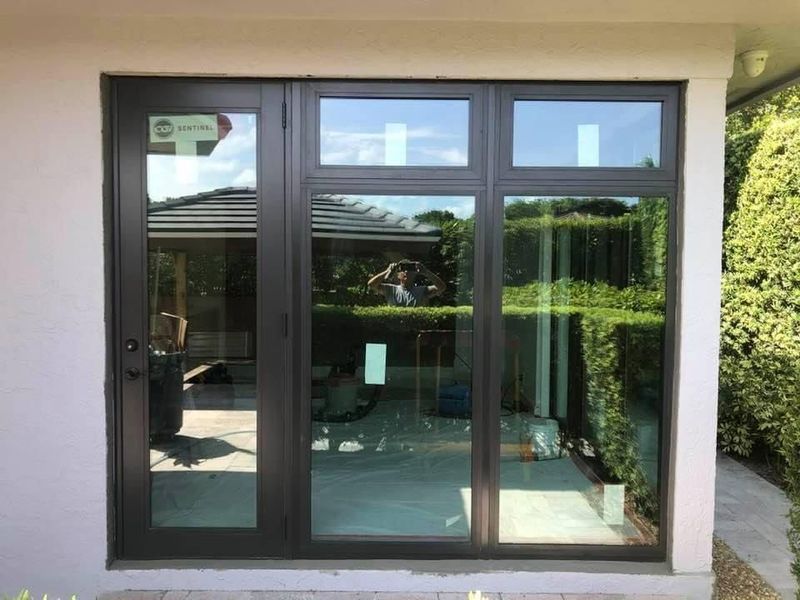 Black framed glass doors and windows, beige exterior, outdoor setting with greenery visible.