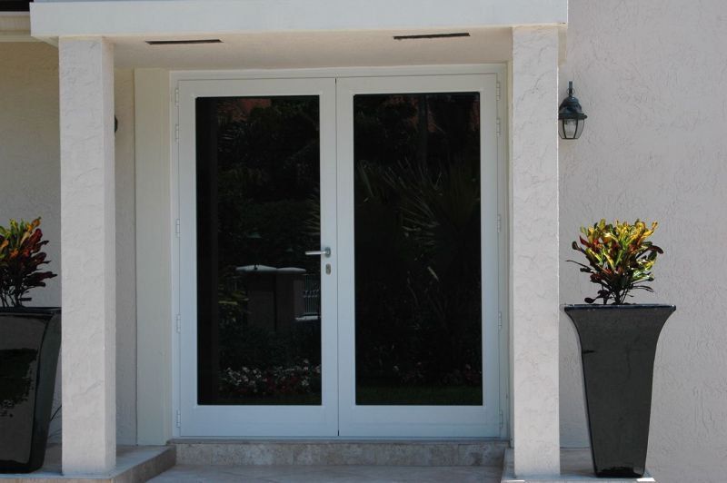 White double doors with dark tinted glass, flanked by planters with colorful plants.