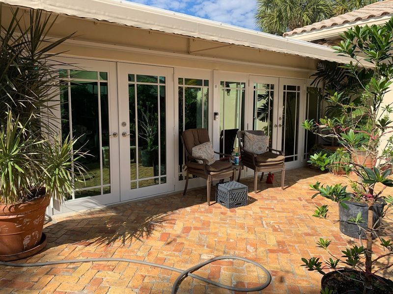 Patio with French doors, brick flooring, potted plants, two chairs, and a small table.