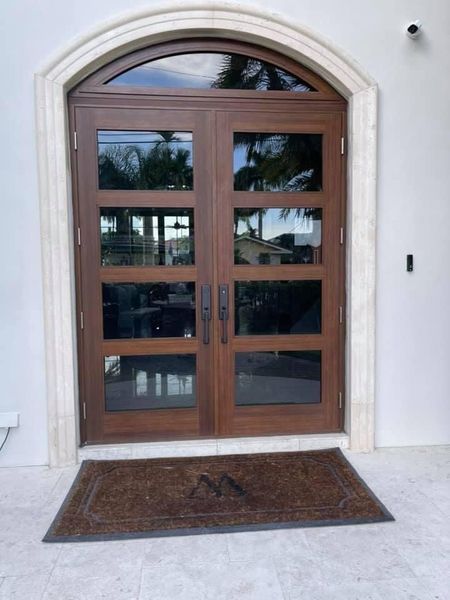 Double wooden door with glass panels set in a white arched doorway. A welcome mat rests in front.