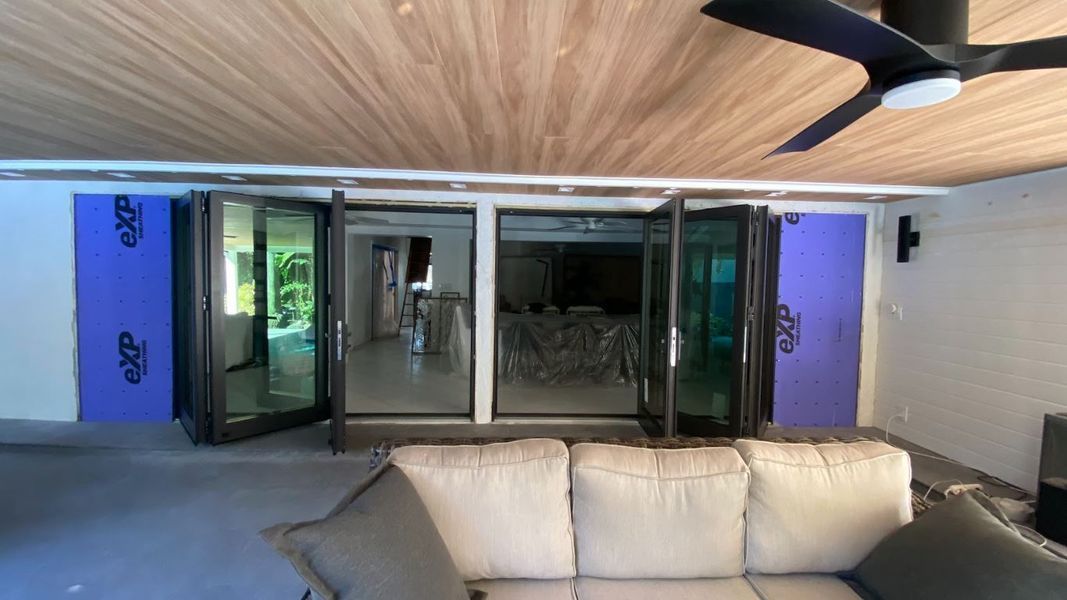 Patio with folding glass doors, couch, purple insulation, wood ceiling, and ceiling fan.