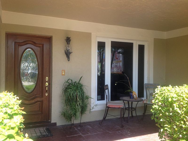 Wooden front door with oval glass panel next to a window with a small table and chairs on a porch.