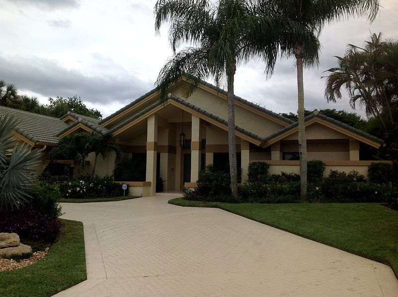 Beige house with a long driveway and palm trees in front.