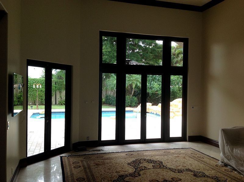 Indoor view of large black-framed doors leading to a pool area. Rug on floor, light-colored walls.