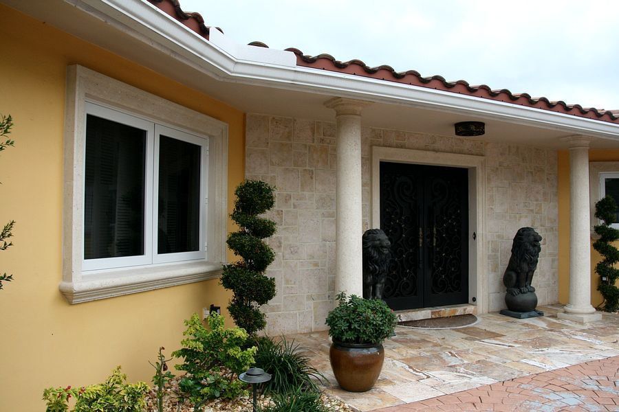 Yellow stucco house with white window and door trim, columns, red tile roof, and ornate black front door.