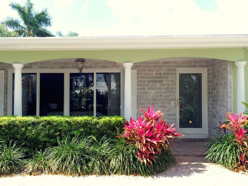 Green and white house exterior with a small porch and colorful landscaping.
