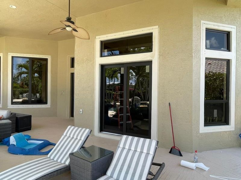 Patio with tan stucco walls, black framed windows, lounge chairs, and a ceiling fan.