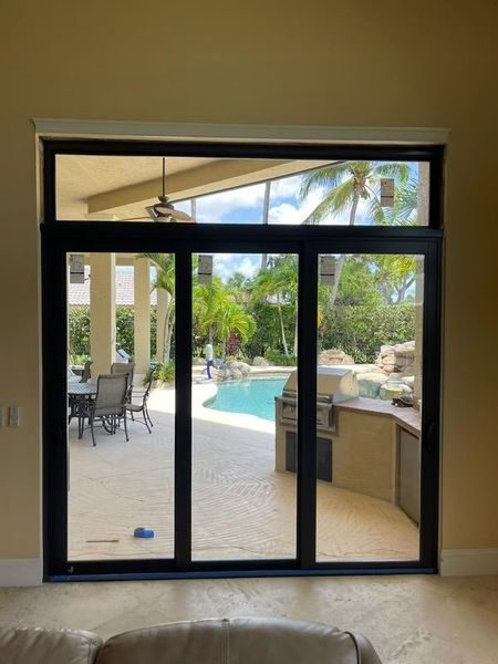 Black-framed glass doors and window overlooking a pool, patio, and outdoor kitchen.