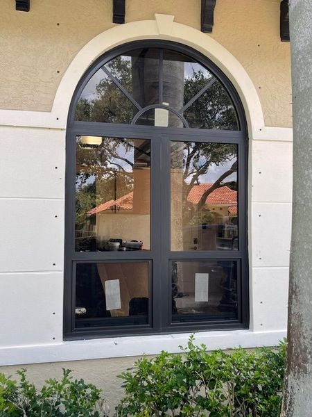 Arched window with black frame, divided into sections. The window is set in a white exterior wall.