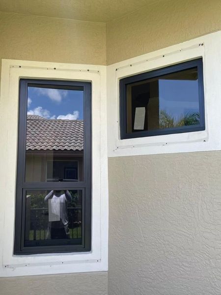 Two dark-framed windows in a corner of a building, reflecting sky and a roof. Cream-colored walls.