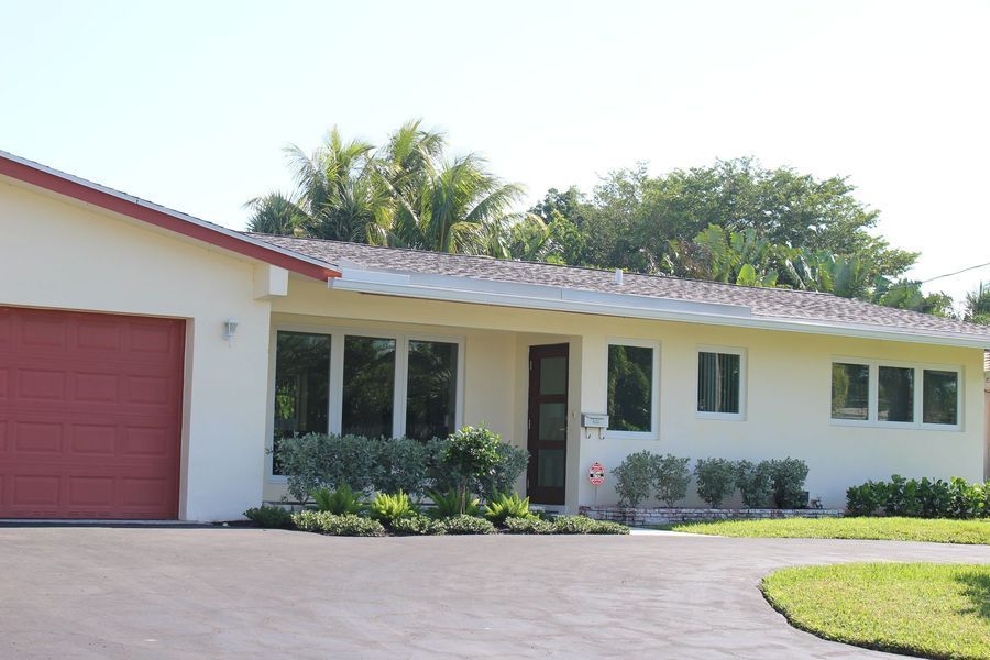 Beige ranch house with red garage door and trim, surrounded by green landscaping and a curved driveway.