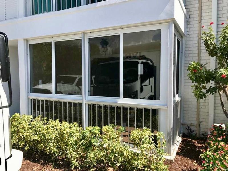 White framed sunroom with glass windows and a metal railing. Cars are parked inside.