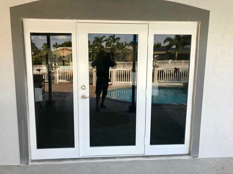 White French doors with tinted glass, reflecting a pool and palm trees. A person is visible in the reflection.