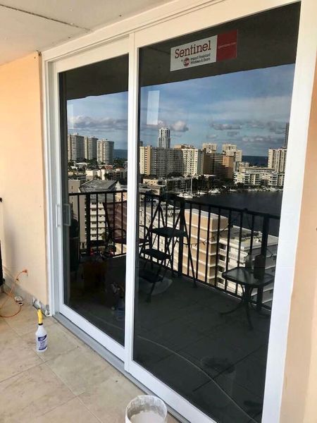 Sliding glass doors with a city view. Doors are white-framed, reflecting the sky and buildings. A balcony is visible.