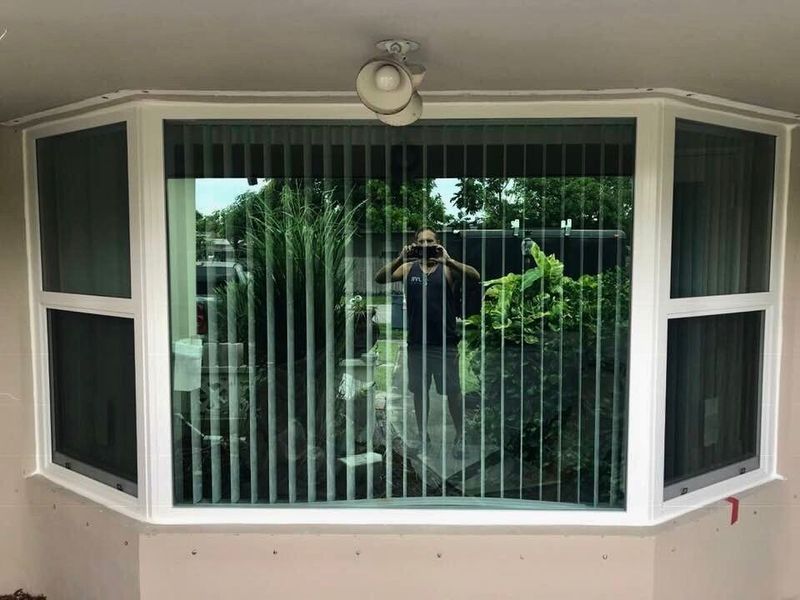 Bay window with white trim, vertical blinds, and a person taking a photo in the reflection.