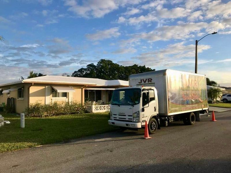 Moving truck parked in front of a house, orange cones on the street, blue sky.