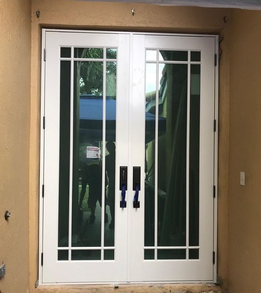 White French doors with glass panes and black handles against a tan wall.