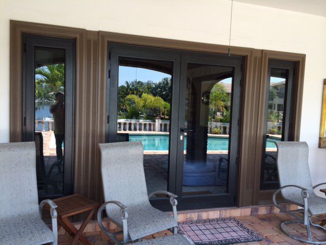 Black-framed glass doors and windows overlook a pool. Patio chairs are in the foreground.