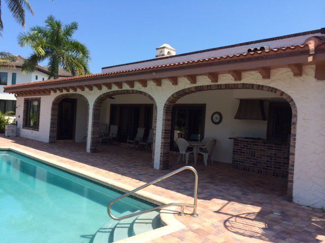 Poolside patio with arched openings, brick details, and a built-in outdoor kitchen.