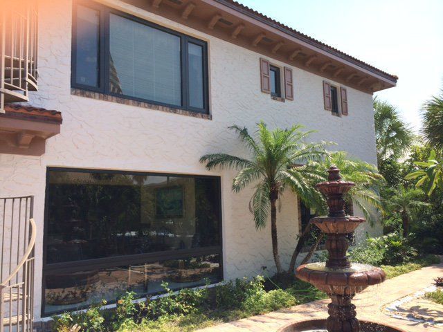 Two-story stucco building with large windows, palm tree, and a fountain in a garden.