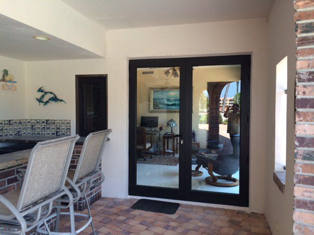 Patio with open black-framed glass doors reflecting interior.  Brick, bar with chairs, and white walls are visible.