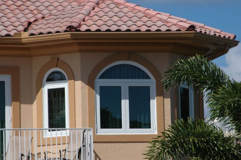 Tan building with white-framed windows, red tile roof, and a palm tree.