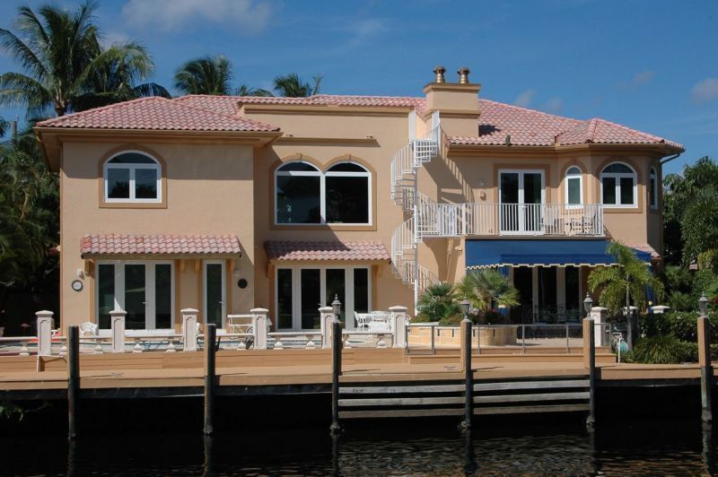 Beige waterfront house with red tile roof, spiral staircase, and blue awning.