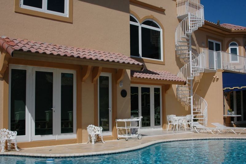 Beige stucco house with pool, spiral staircase, white doors, and red tile roof.