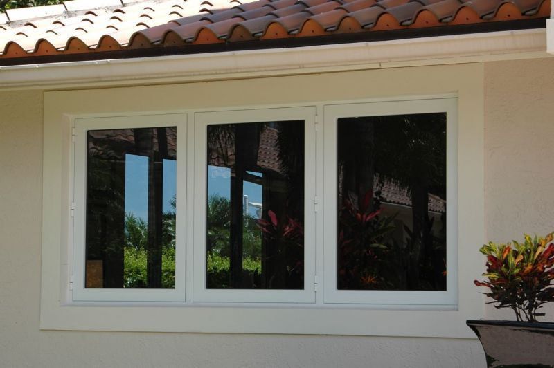White-framed triple window reflecting trees and sky against a light-colored stucco wall under a terracotta roof.